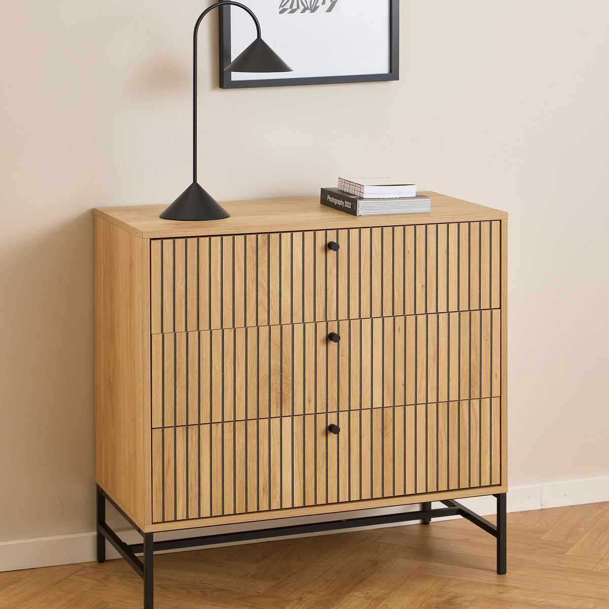 Bambouz-kommode 81x81 foran et vægmaleri med en sort lampe og bøger – en lamellkommode til stuen