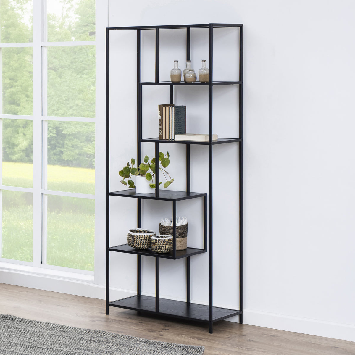 Skeleto-reol 77x185 i sort melamin ved et stort vindue med en plante, kurve og bøger – sort reol til stuen