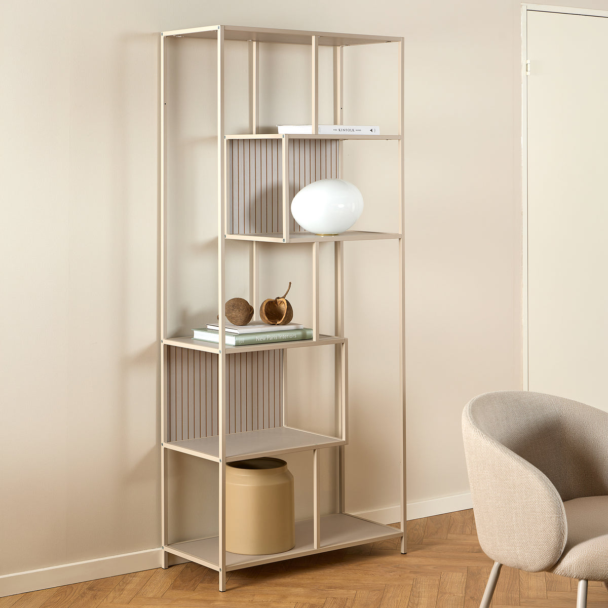 Skeleto-reol 77x185 i grå melamin i et lyst rum ved siden af en lænestol, med en kugleformet lampe – en reol til stuen