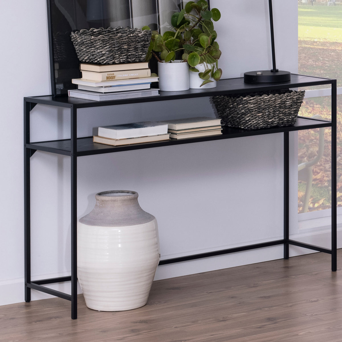 Skeleto-konsol 120x79, sort melamin, placeret op ad væggen med kurve, bøger og en plante, med en vase nedenunder