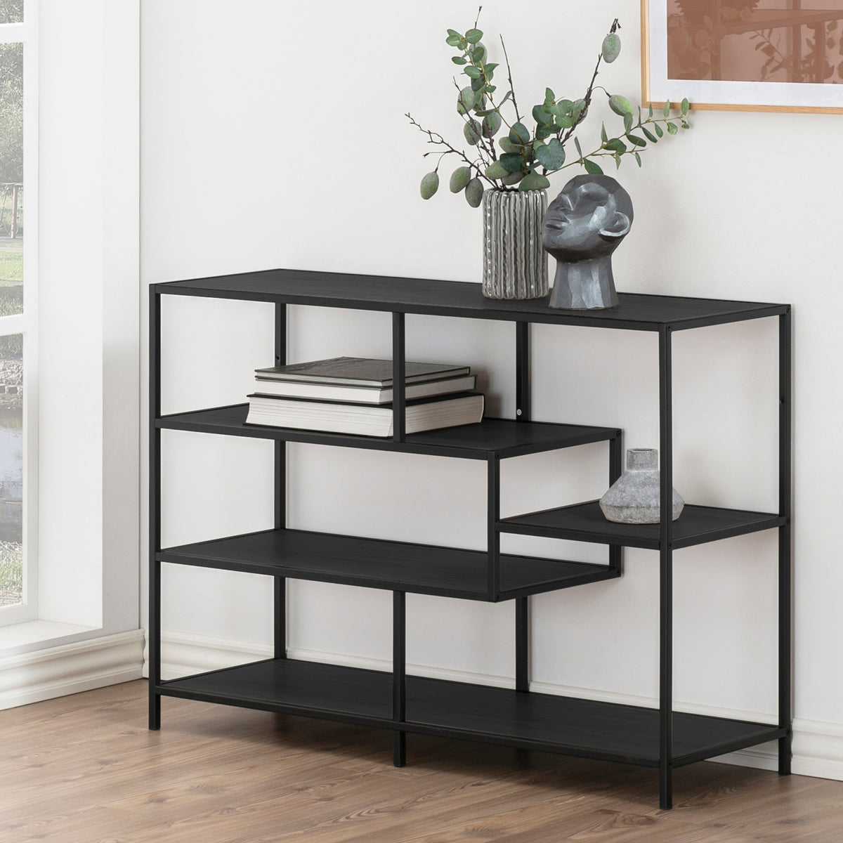Skeleto-reol 114x78 i sort melamin ved vinduet med kviste i en vase, en skulptur og bøger – sort reol til stuen