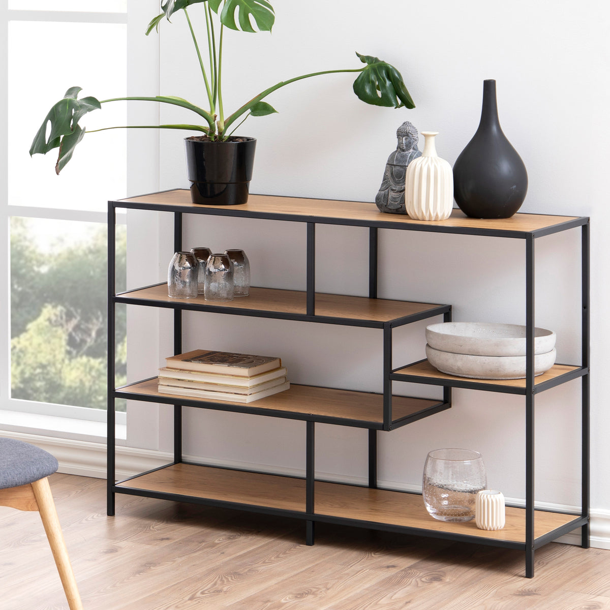 Skeleto-reol 114x78 i vild eg i en lys stue ved vinduet, med en plante, vaser og bøger – en reol til stuen