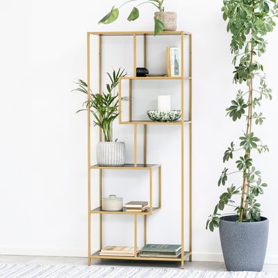 Skeleto-reol 77x185 i sort melamin (guldramme) ved en hvid væg omgivet af planter i krukker – en glamourøs reol