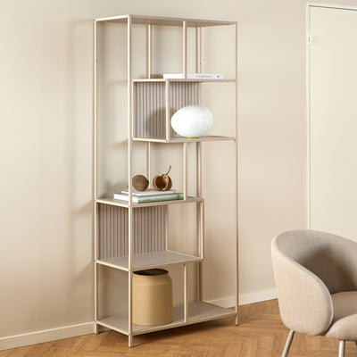 Skeleto-reol 77x185 i grå melamin i et lyst rum ved siden af en lænestol, med en kugleformet lampe – en reol til stuen