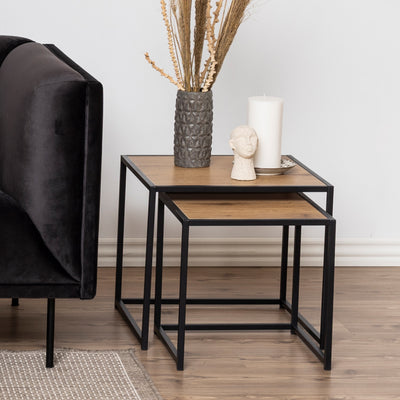 Skeleto-sofaborde 50x45 i rå eg ved siden af en mørk veloursofa, med en vase og et lys – sofaborde til stuen