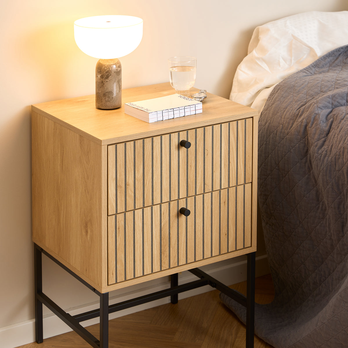 Bambouz-natbord 46x70 i soveværelset ved siden af sengen med en lampe, bøger og et glas – natbord med skuffer